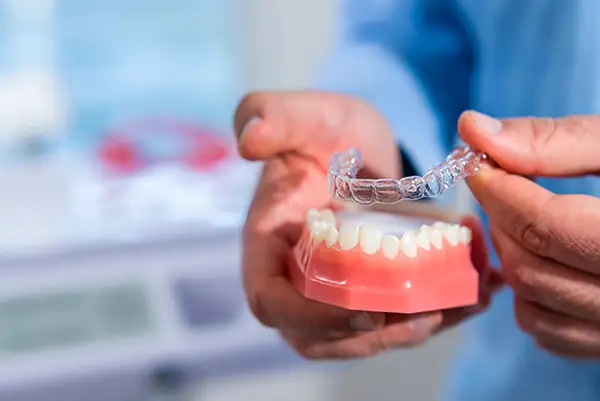 Close-up of a hand holding a clear aligner above a dental model, demonstrating how the aligner fits over teeth.
