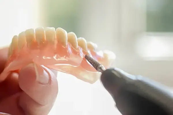 Close-up of a dental professional using a tool to adjust and customize a set of dentures for a patient.