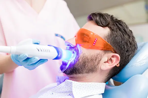 A dentist holds a UV light to a patient's teeth during a teeth whitening procedure.