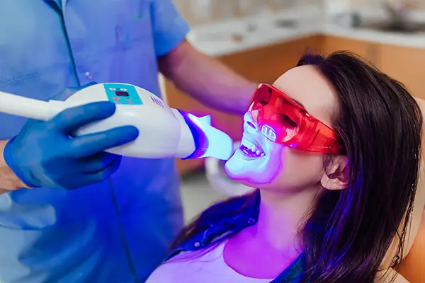 A hygienist uses a whitening instrument on a female patient going through teeth whitening treatment.