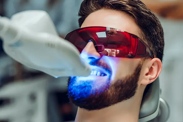 A patient having his teeth whitened by a dental UV whitening device, his eyes protected with glasses.